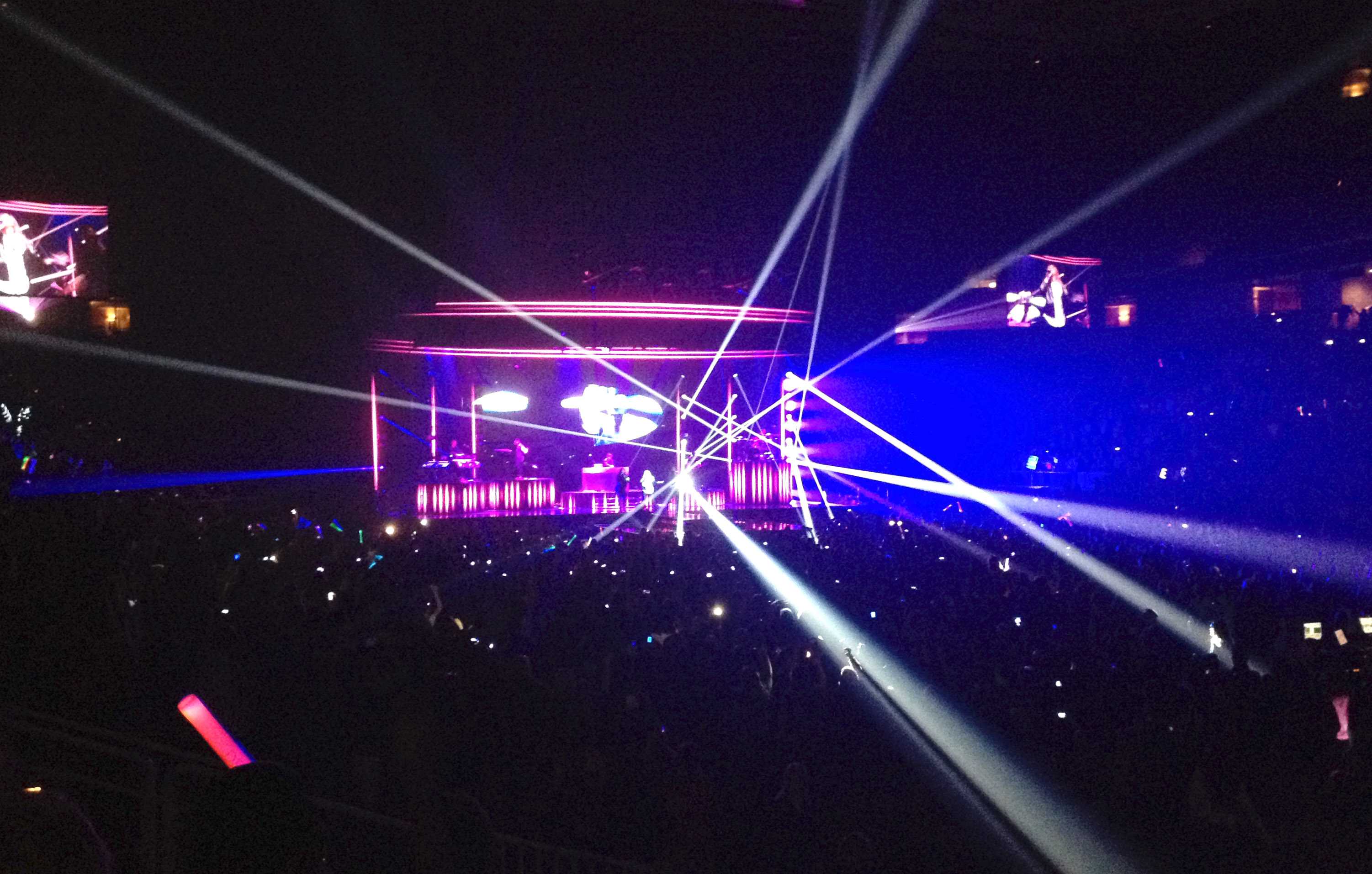 Demi Lovato sings on stage while the stage lights shine into the crowd.
